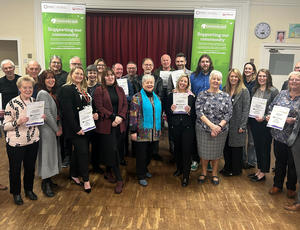 Groups of around 25 people holding certificates, with green EnviroGrant branded banners in the background