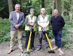 Photo showing volunteers Julie and Chris each holding a tree popper tool (which are a yellow metal rod 1 metre tall with a black semi circular part on the end), in Apley Woods with Councillor Overton and Ian Hancock from Veolia