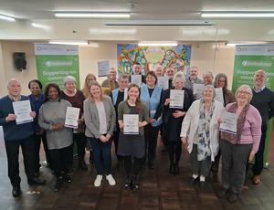Photo showing a large group of people with grant certificates, in a community hall with EnviroGrant branded banners in the background