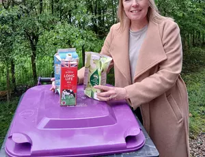 Person holding cartons next to a purple lidded wheelie bin
