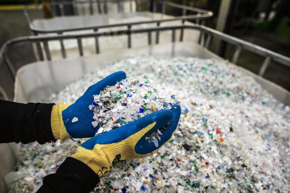 Image of gloved hands holding shredded plastics at a recycling facility