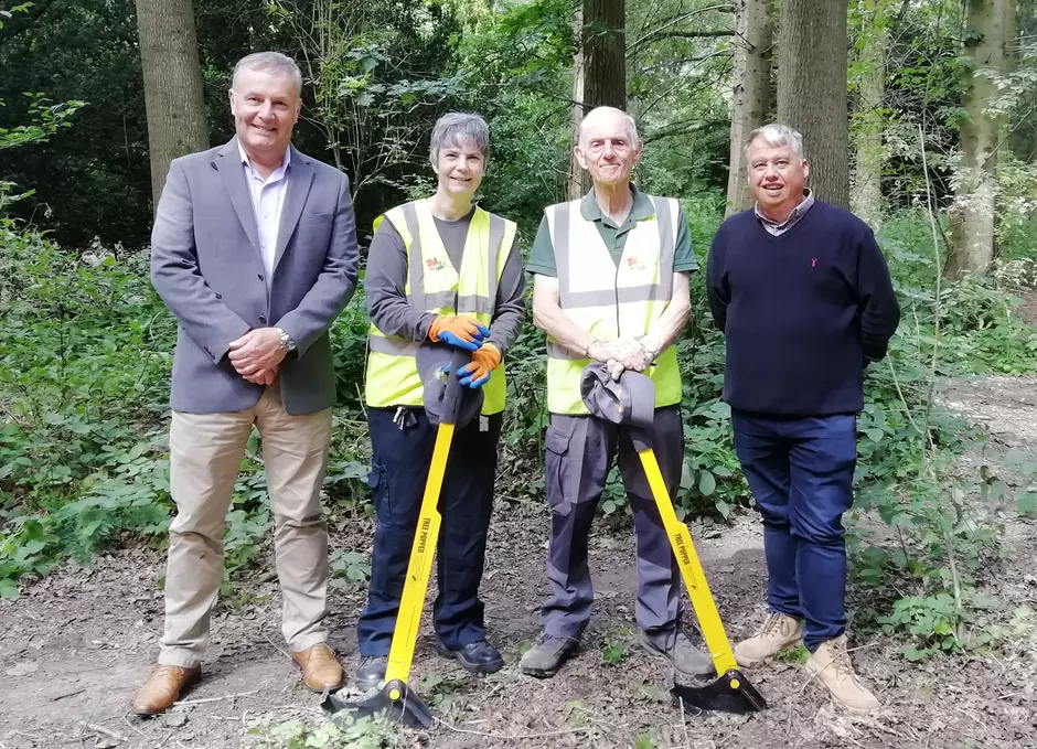 Photo showing volunteers Julie and Chris each holding a tree popper tool (which are a yellow metal rod 1 metre tall with a black semi circular part on the end), in Apley Woods with Councillor Overton and Ian Hancock from Veolia