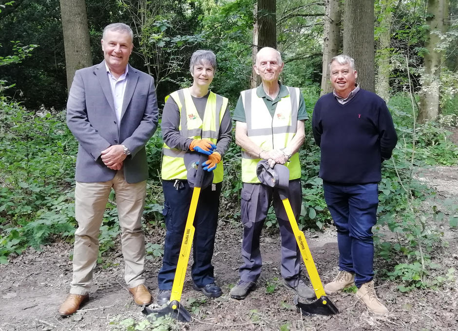 Photo showing volunteers Julie and Chris each holding a tree popper tool (which are a yellow metal rod 1 metre tall with a black semi circular part on the end), in Apley Woods with Councillor Overton and Ian Hancock from Veolia