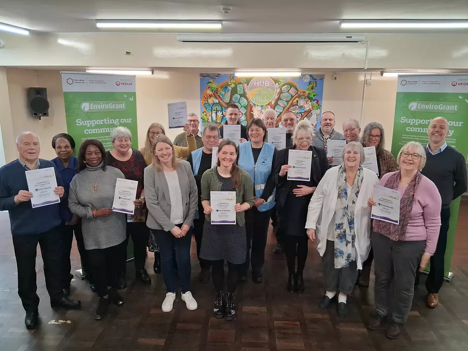 Photo showing a large group of people with grant certificates, in a community hall with EnviroGrant branded banners in the background