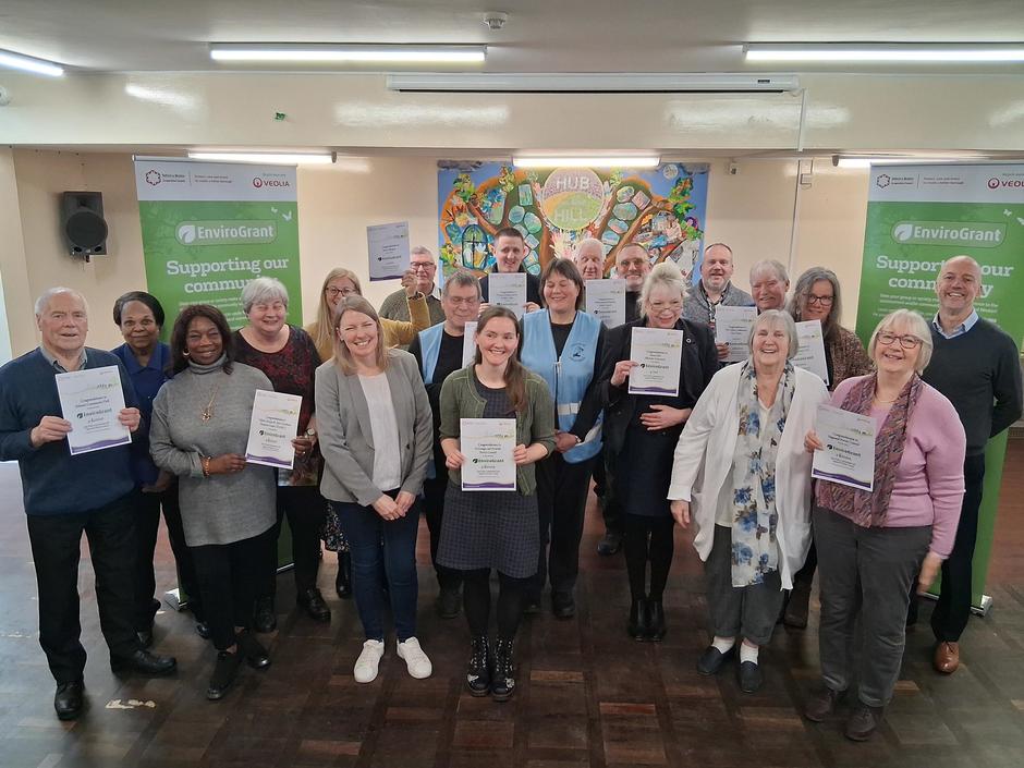 Photo showing a large group of people with grant certificates, in a community hall with EnviroGrant branded banners in the background