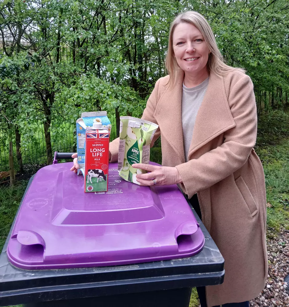 Person holding cartons next to a purple lidded wheelie bin