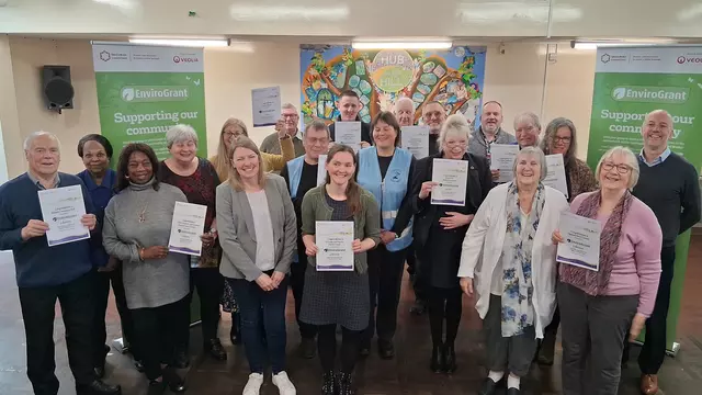 Photo showing a large group of people with grant certificates, in a community hall with EnviroGrant branded banners in the background
