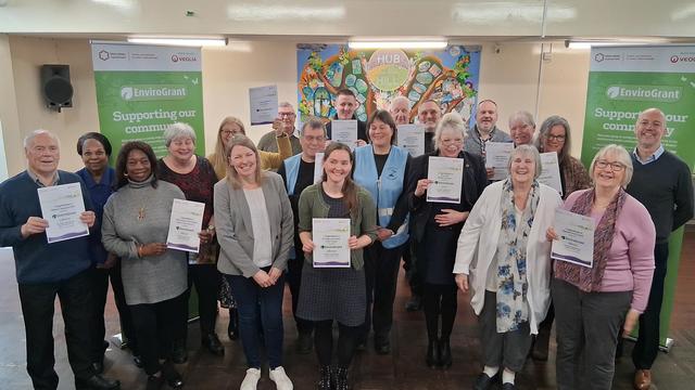 Photo showing a large group of people with grant certificates, in a community hall with EnviroGrant branded banners in the background